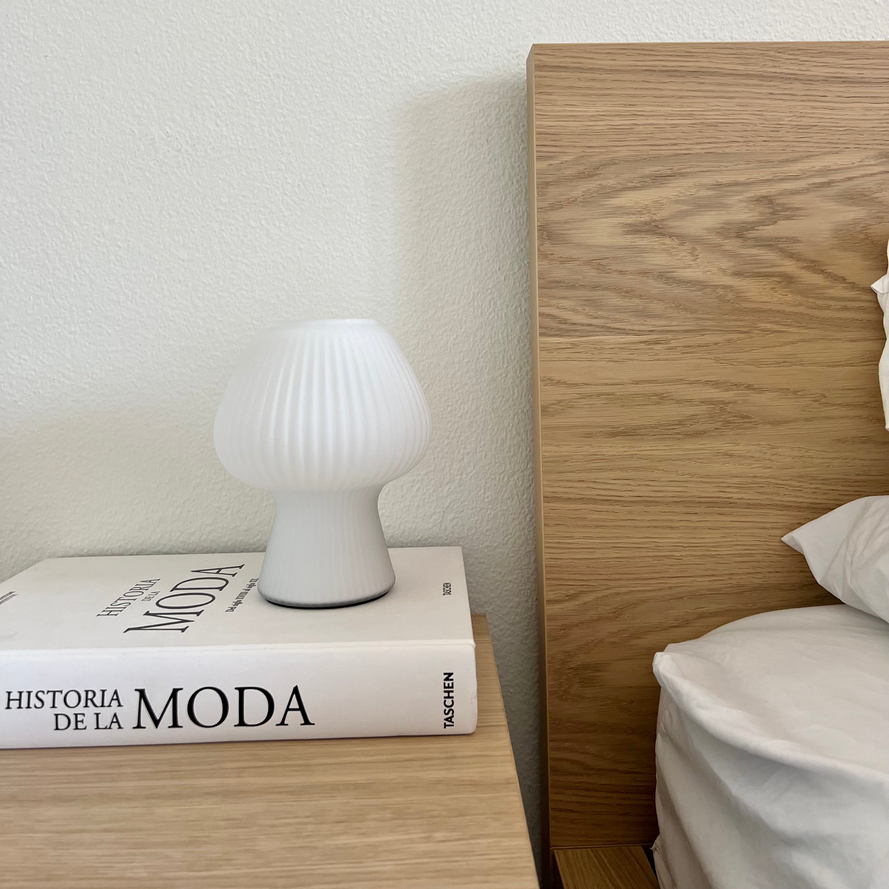 White mushroom lamp on a book next to a wooden bed frame.